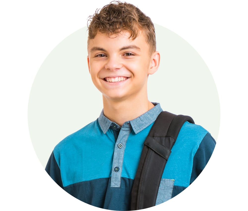 A young blonde boy is smiling. He has a backpack slung over his shoulder.