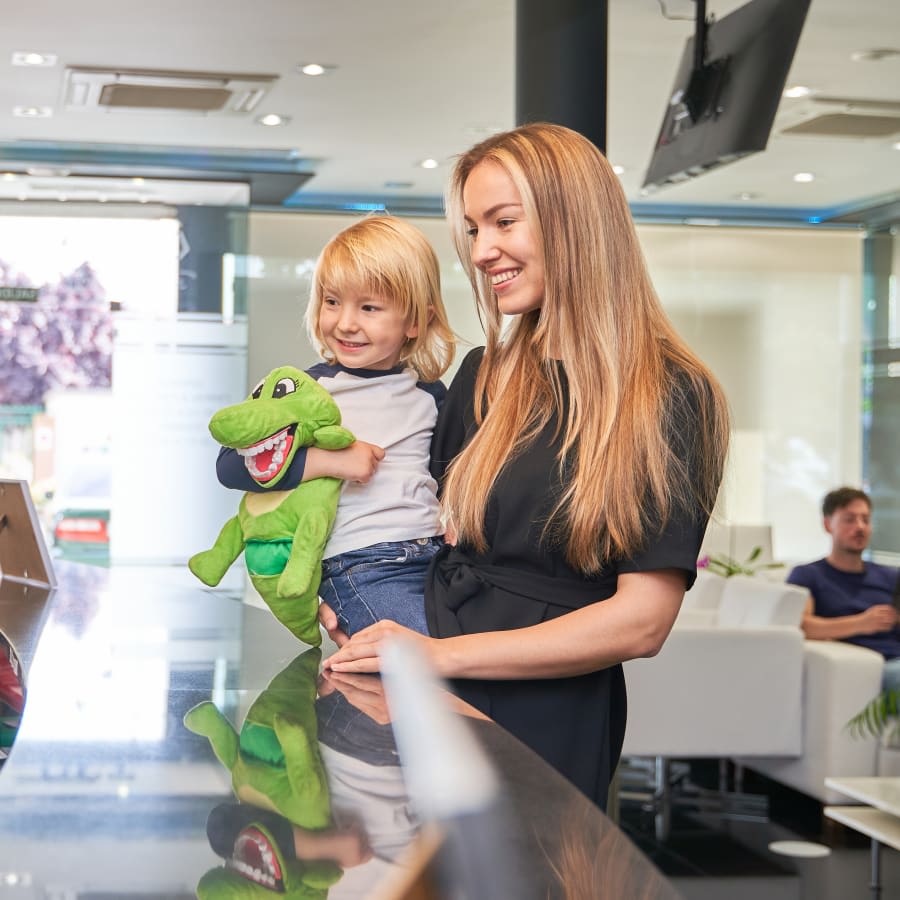 A mother holds her child at a reception desk. The child is holding a stuffed animal of an alligator.